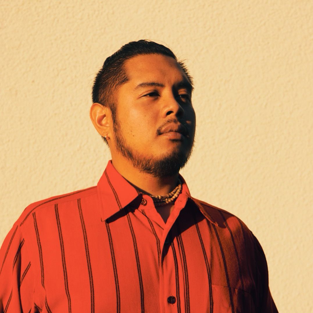 Portrait of Jamil Apostol in a red striped shirt against a warm cream wall